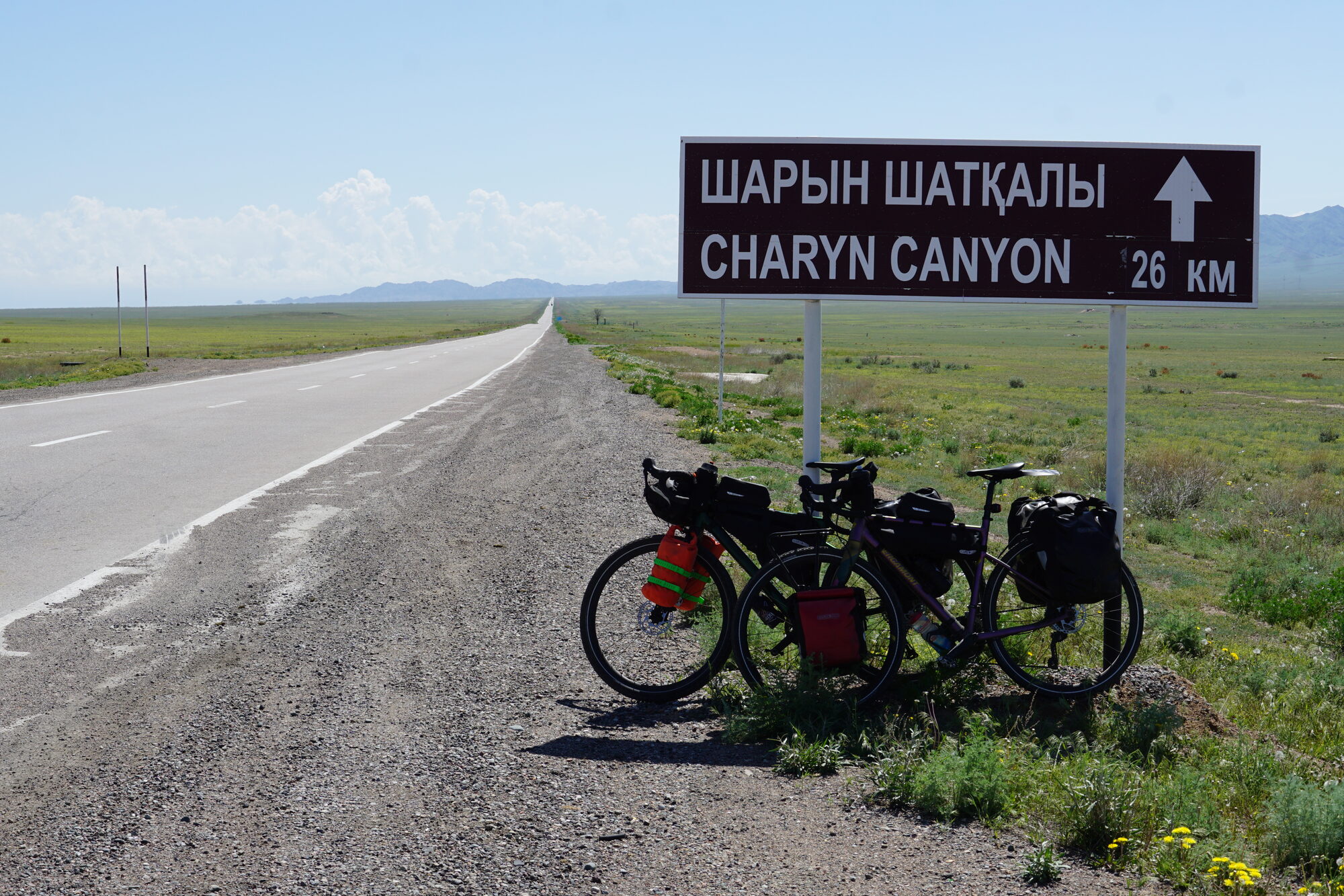 Unsere Räder vor einem Straßenschild und einer langen geraden Straße richtug Charyn Canyon